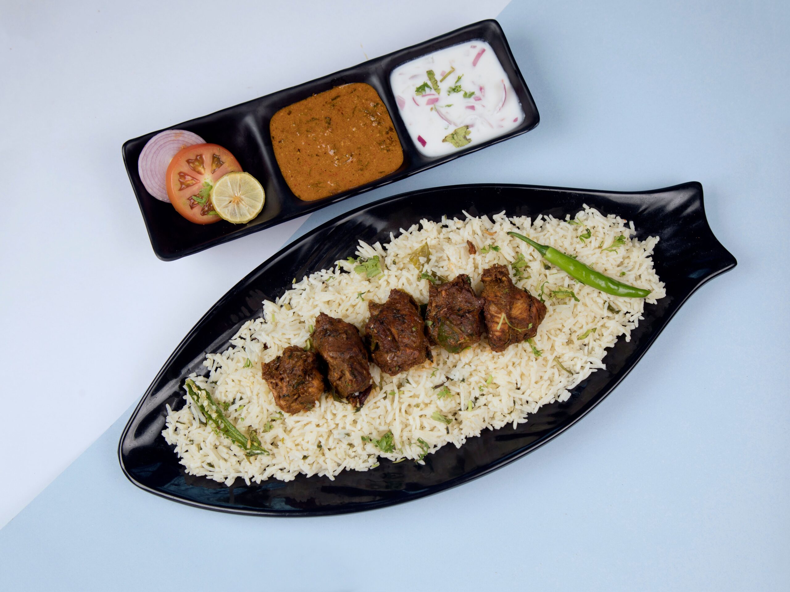 A flavorful plate of lamb biryani served with raita, curry, and salad on the side.